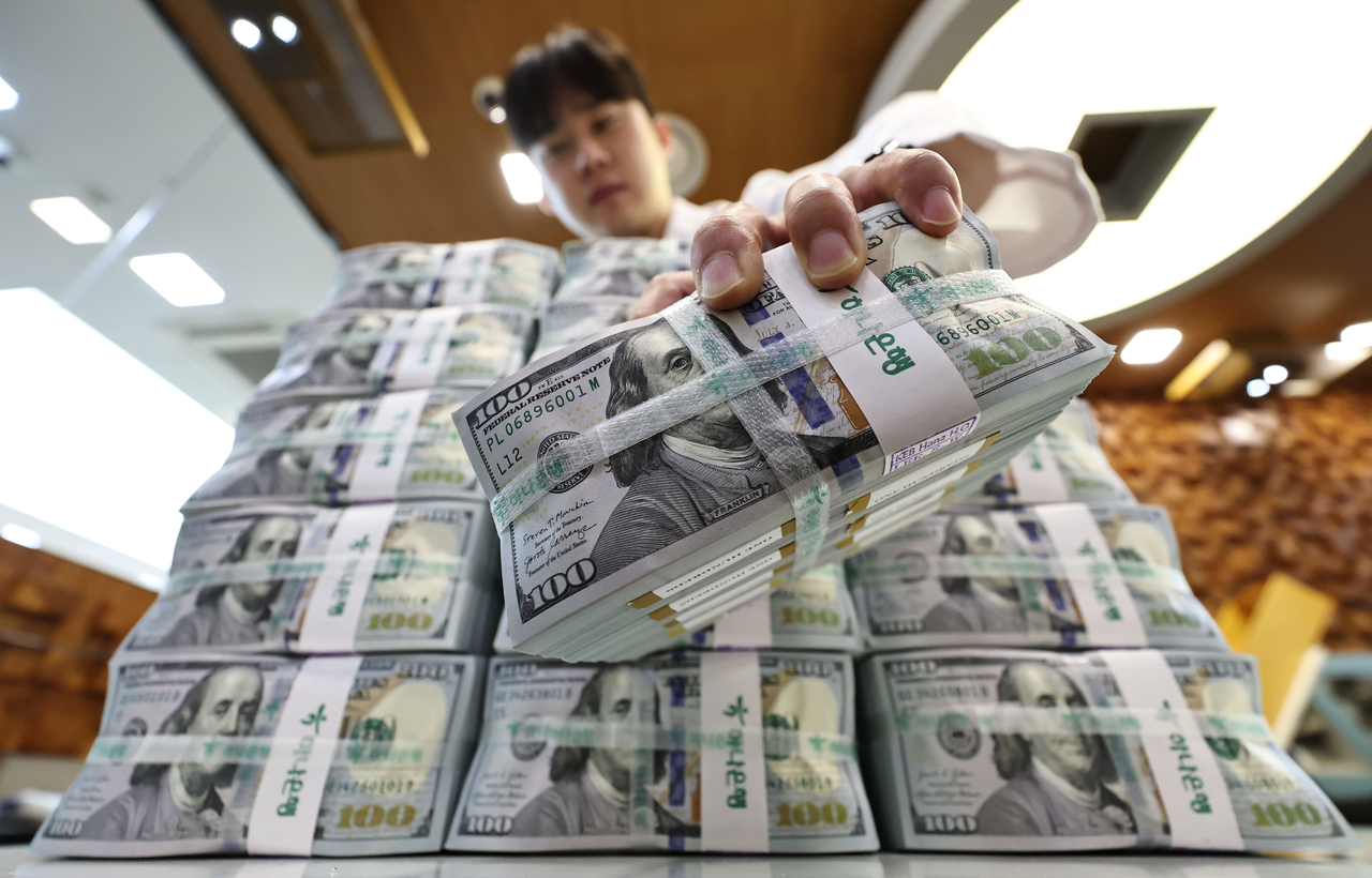 An employee at Hana Bank holds up a bundle of US dollars on Sept. 3. (Yonhap)
