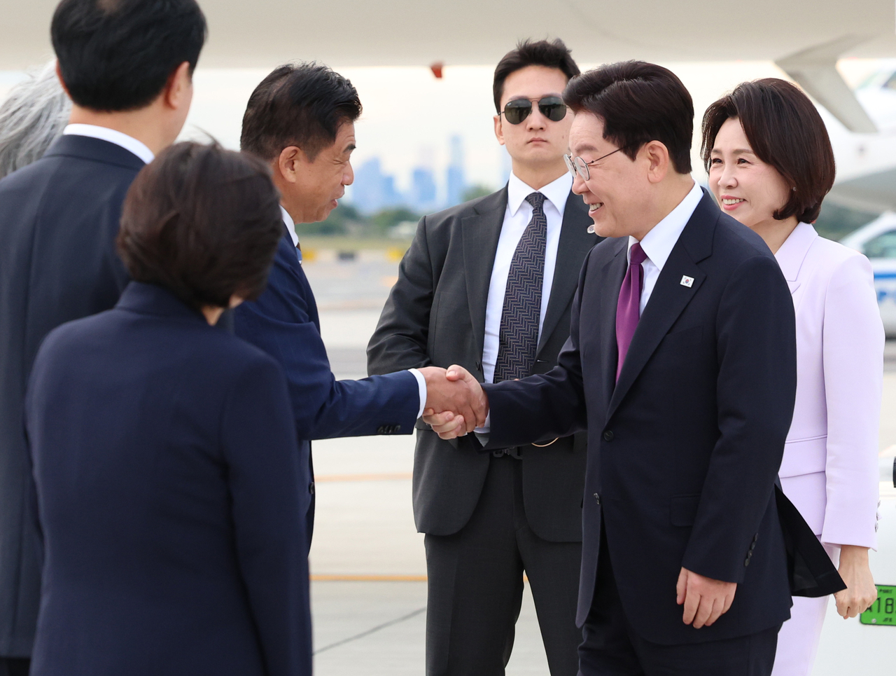 이재명 대통령과 김혜경 여사가 21일(현지시간) 미국 뉴욕 JFK 국제공항에서 영접 나온 차지훈 주유엔대사와 인사하고 있다. [연합]