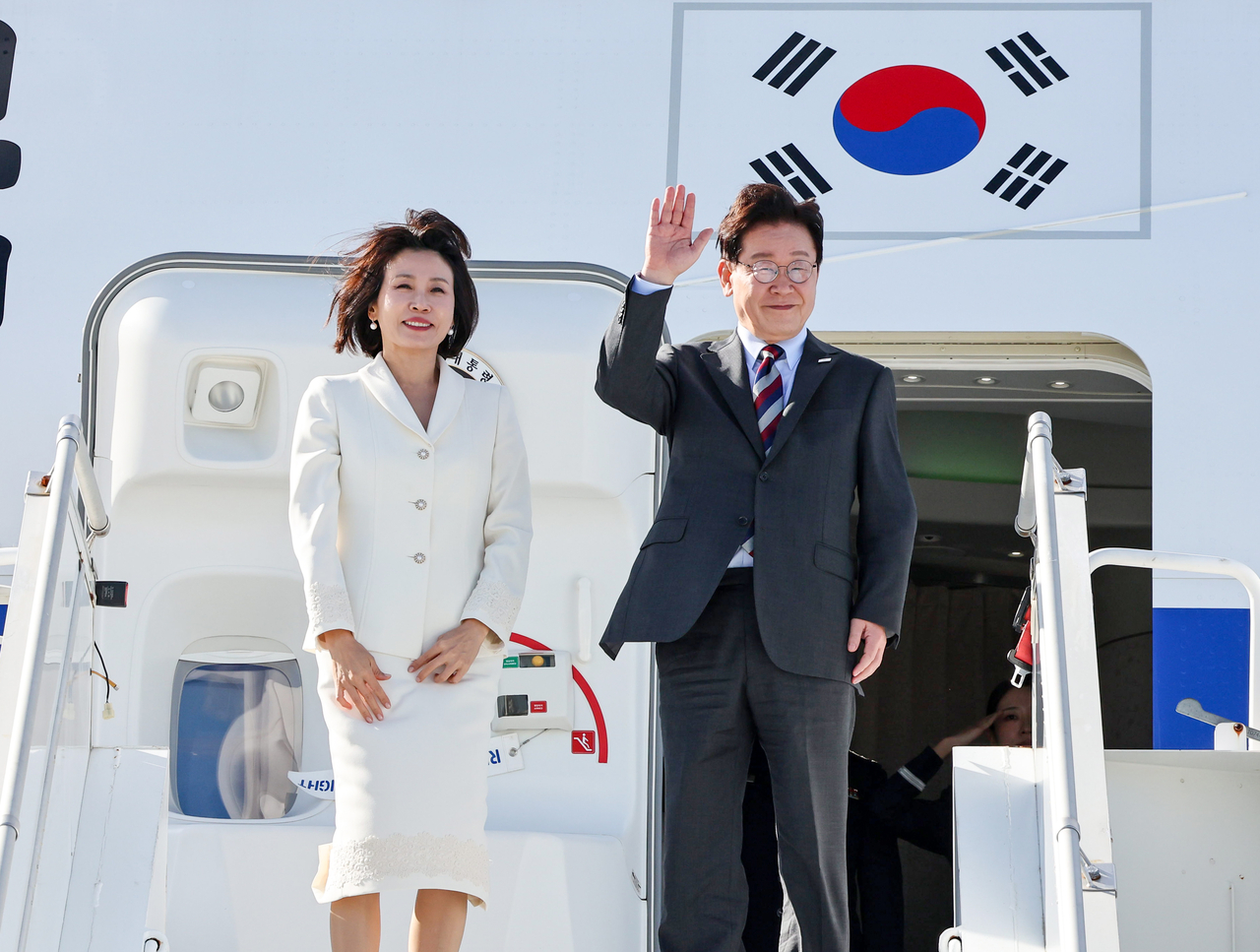 President Lee Jae Myung and first lady Kim Hye-kyung wave to well-wishers from Air Force One at John F. Kennedy International Airport in New York on Wednesday (local time), as they depart for a state visit to Mexico after completing their US schedule. [Yonhap]