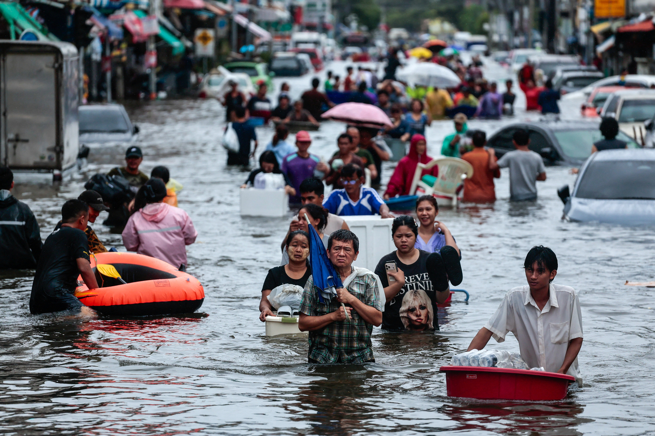People wade through a flooded area during heavy rain in Bangkok on Sunday. (Reuters-Yonhap)