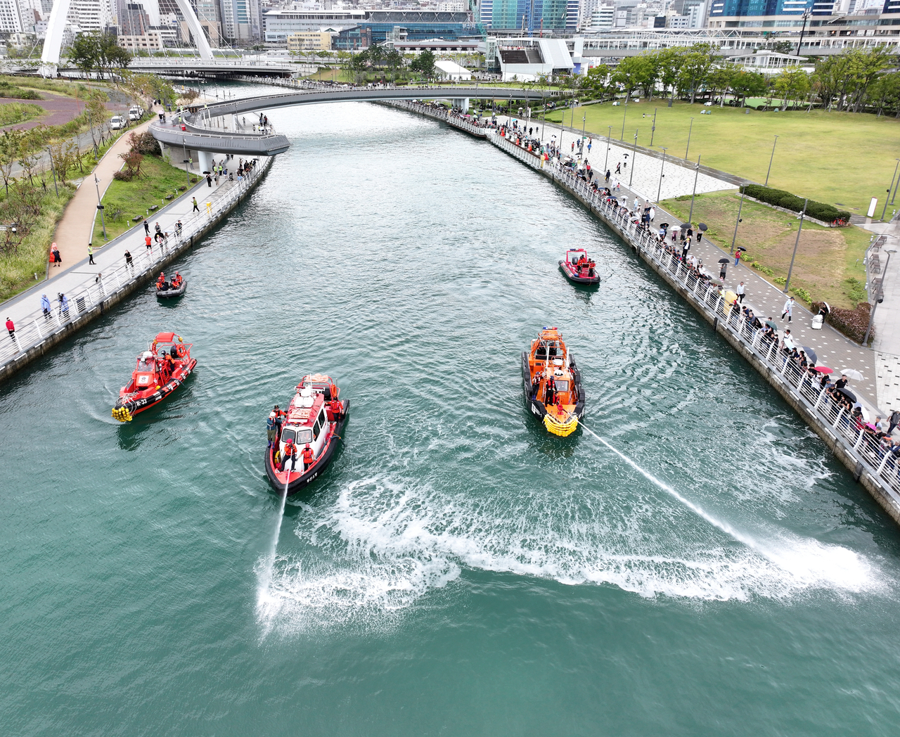 Coast Guard vessels spray water from water cannons in a bid to steer a shark toward the open sea on Tuesday as people watch at a waterfront park in Busan. (Yonhap)