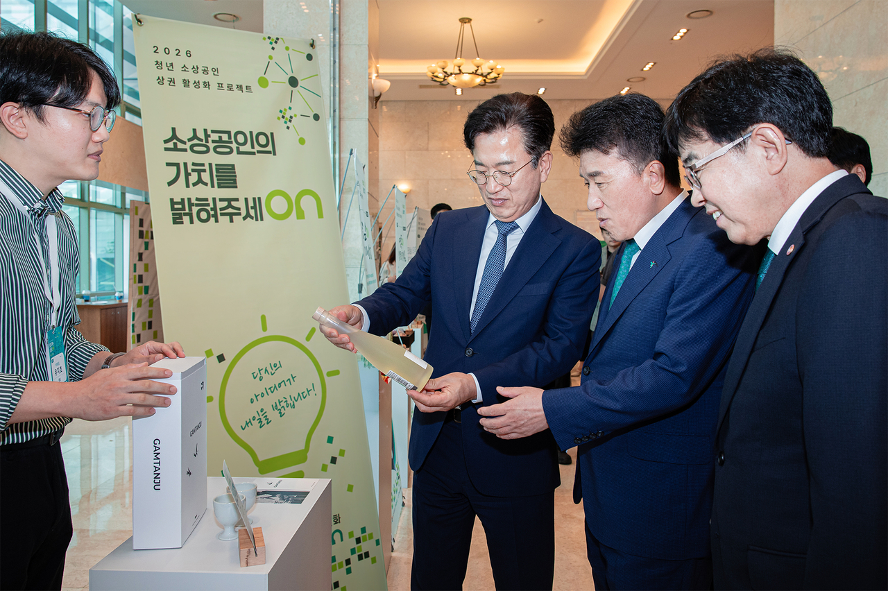 Hana Financial Group Chairman Ham Young-joo (second from right) and Small Enterprise and Market Service President In Tae-yeon (third from right) examine products showcased at the launch ceremony for a youth merchant commercial district revitalization project in Daejeon on Tuesday. (Hana Financial Group)