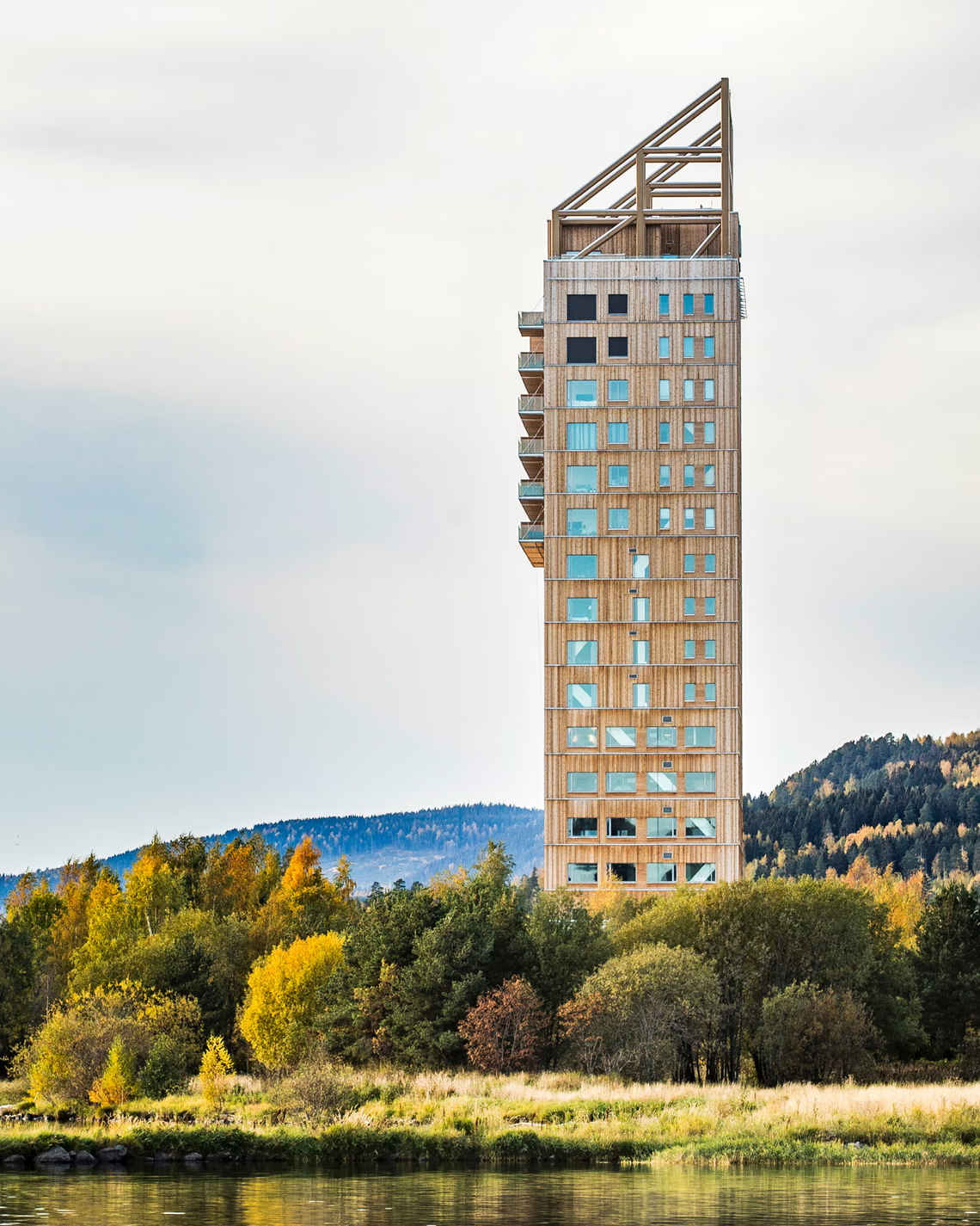 Mjøstårnet, an 18-story timber high-rise standing on the shore of Lake Mjøsa in Brumunddal, Norway. Rising about 84 meters, the building uses engineered wood — including glued laminated timber — as its primary structural material. Timber high-rises that replace concrete and steel to cut construction emissions are gaining ground across Europe. [The Guardian]