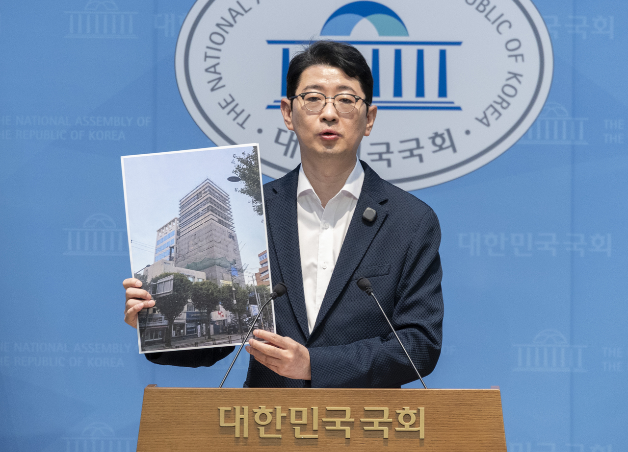 People Power Party lawmaker Ju Jin-woo holds up a photo of a building under construction in Mapo-gu, Seoul, near Hongdae during a press conference at the National Assembly on Sunday, where he raised allegations that funds invested by Korea Development Bank and Industrial Bank of Korea were used to build the new headquarters of Hive MEDIAcorp, the production company behind "The Assassin." [Yonhap]
