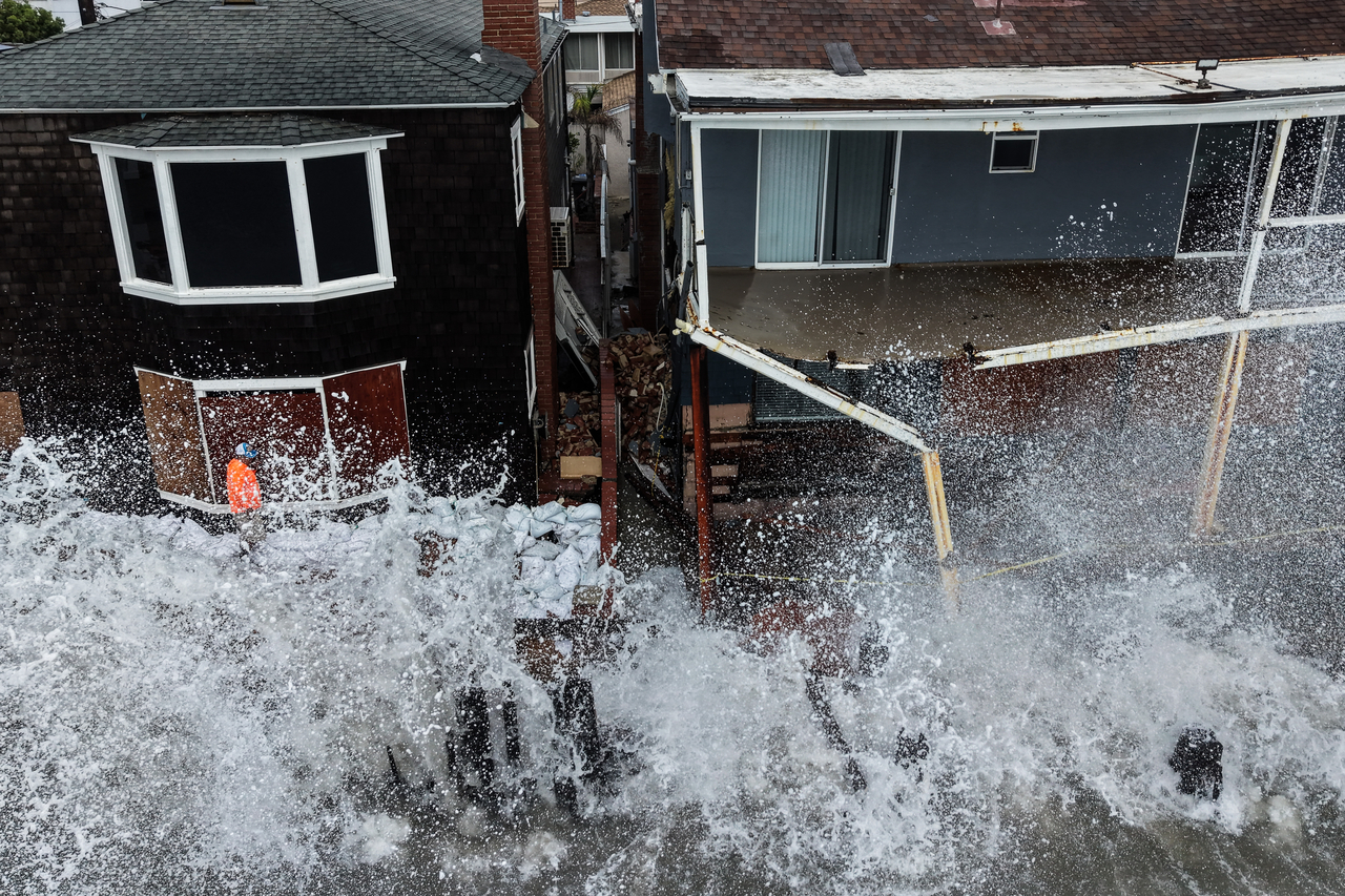 A worker stands next to a stack of sandbags as waves crash into homes in Long Beach, California, Monday. (AP-Yonhap)