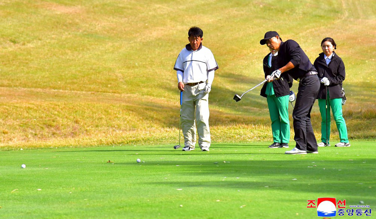 A man hits a golf ball near the green at the Pyongyang Golf Course as fellow players watch behind him, in this photo released Friday. (KCNA via Yonhap)