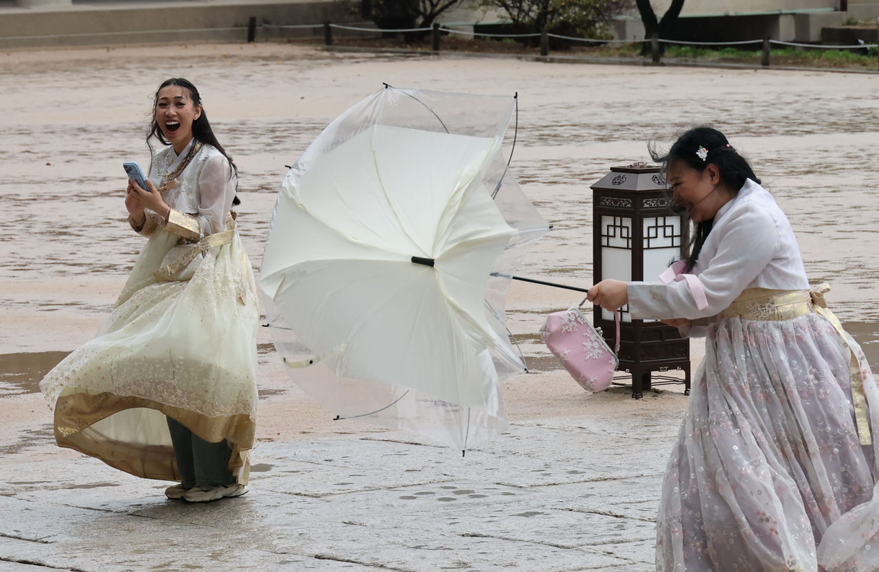 Tourists wearing hanbok brave heavy rain and strong winds at Gyeongbokgung in Jongno-gu, Seoul, Sunday. (Yonhap)