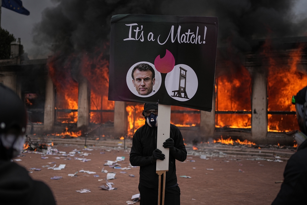 A protester holds a board with a photo of French president Emmanuel Macron in front of a burning tourism office during a demonstration in Lyon, France, Saturday. (AP-Yonhap)