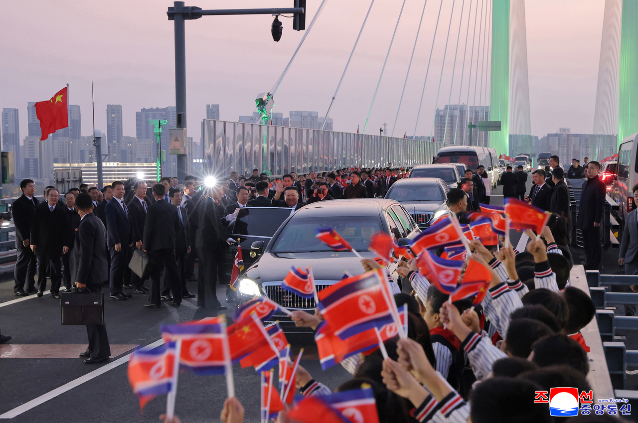 North Korean leader Kim Jong-un crosses into China via the New Amnok River Bridge as people wave North Korean flags to welcome him on Oct. 24, in this photo released by the Korean Central News Agency on Sunday. (KCNA)