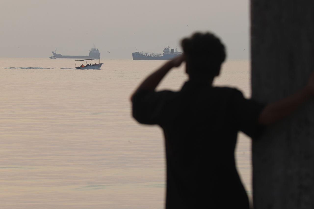 A man watches a small boat pass between cargo vessels anchored in the Strait of Hormuz near Bandar Abbas, Iran, on Saturday (local time). [AP]