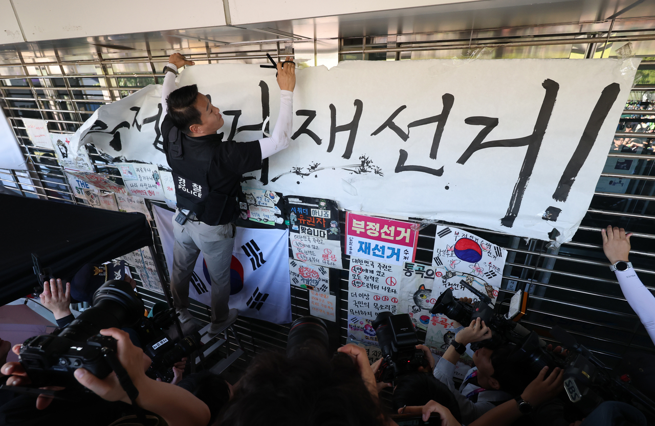 This file photo, taken Sept. 8, shows a police officer taking down a banner calling for a rerun of the June 3 local elections at the Olympic Park Handball Gymnasium in southeastern Seoul. (Yonhap)