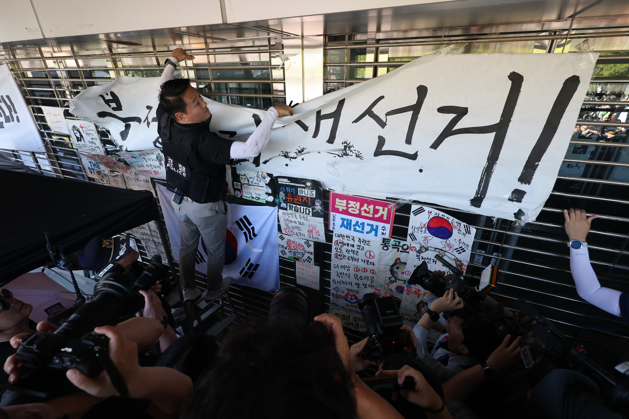 In this file photo, a police officer takes down a banner demanding a rerun of elections at the Olympic Park Handball Gymnasium in southeastern Seoul on Sept. 8. (Yonhap)