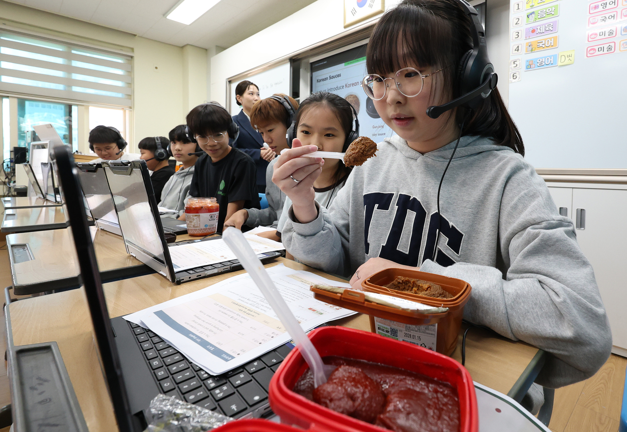 Kim Ha-jin (right), a sixth grader at Seoul Beondong Elementary School in Seongbuk-gu, holds up a spoonful of doenjang, a traditional Korean fermented soybean paste, while introducing Korean sauces to students in Indonesia and Japan during a virtual international class on Tuesday. (Newsis)