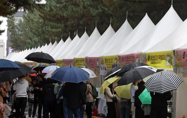 Visitors holding umbrellas browse festival booths at the Gangneung Coffee Festival on the coffee street in Gangneung, Gangwon Province, on Sunday.