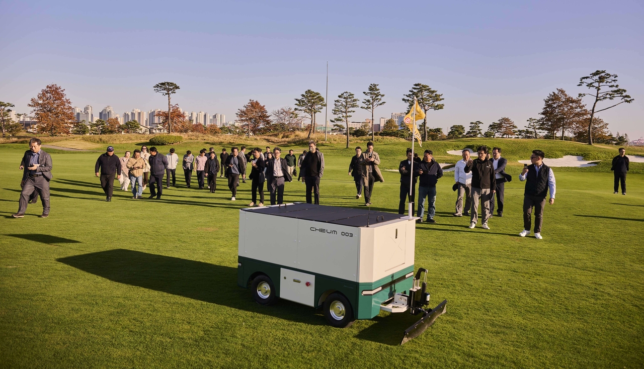 Attendees watch the autonomous divot-repair robot carry out its restoration process during a field demonstration. [HL D&I Halla]