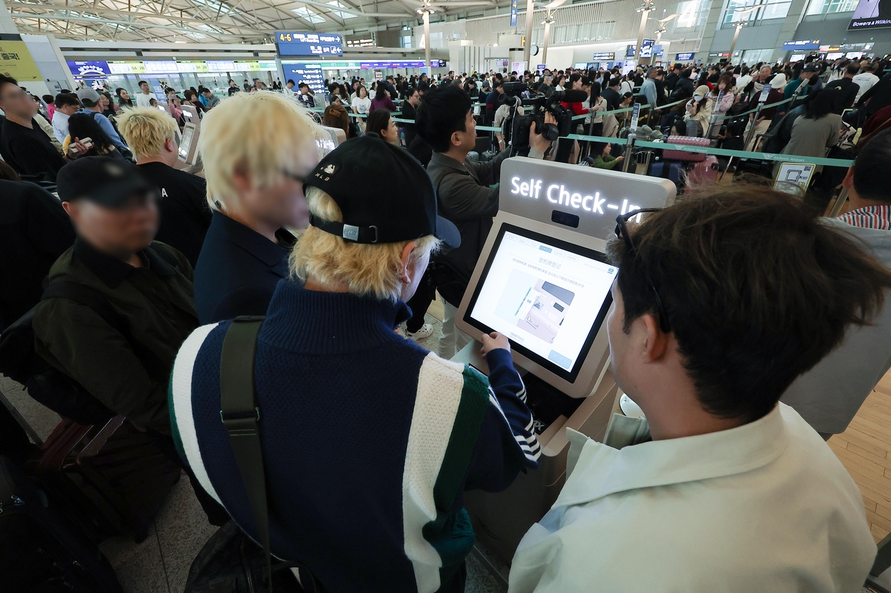 Passengers try to use self-service check-in kiosks at Incheon Airport’s Terminal 1 on Friday after a network disruption affected three airlines’ ticketing operations. (Yonhap)