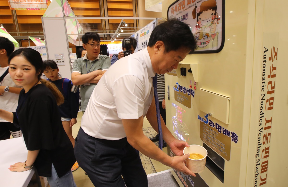 A man pulls out a bowl of ramen from a ramen vending machine, similar to a pressure cooker, at the Ramen Fair held at Coex Convention and Exhibition Center on Sunday. (Yonhap)