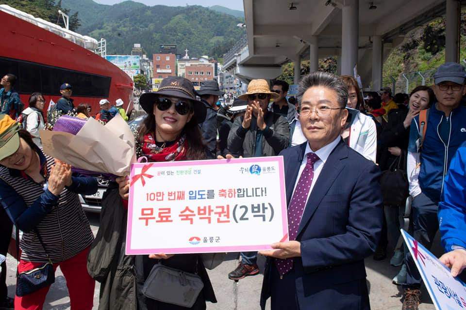김병수 울릉군수(오른쪽)가 10만째 관광객으로 선정된 김가윤(50)씨에게  무료숙박권을 전달하며 축하하고 있다.(울릉군 제공)