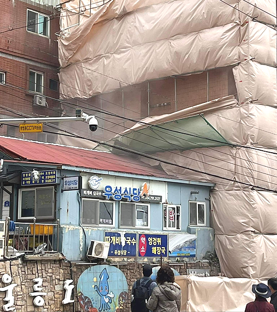 지난 15일 오전 11시 45분쯤 울릉군 울릉읍 도동리 여객선 터미널 인근에 위치한 5층 짜리 건물 철거 공사 현장에서 건물 일부가 무너지고 있는 모습을 주민들이  지켜보고 있다(독자 제공)